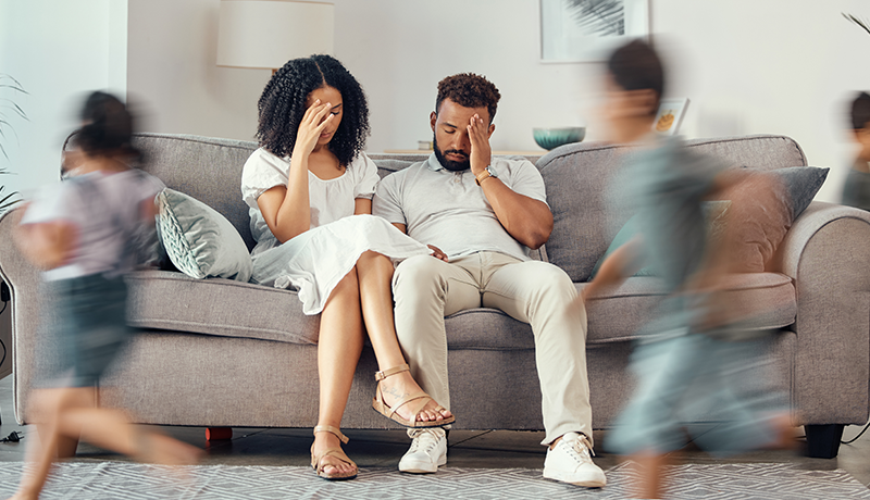 stressed couple on couch and blurred kids running